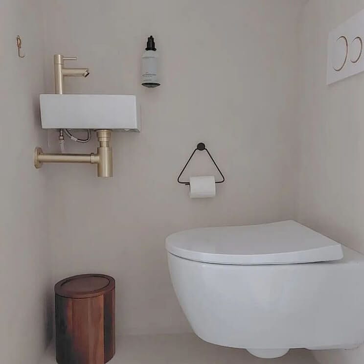 Strakke badkamer met hangend toilet en gouden fonteinset